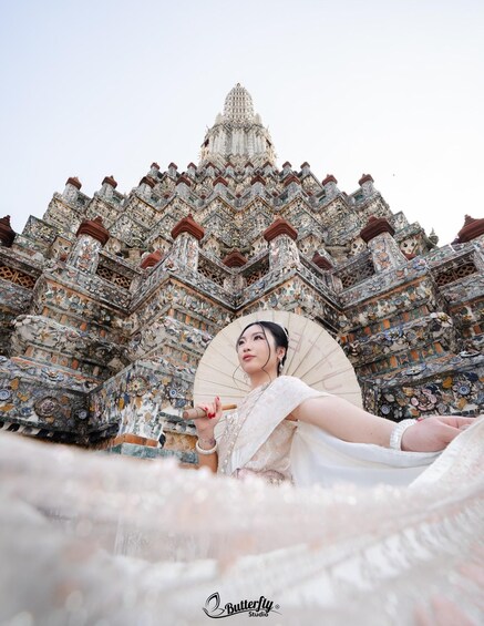 A person in traditional attire with a fan, standing in front of a detailed temple with ornate architecture. 3