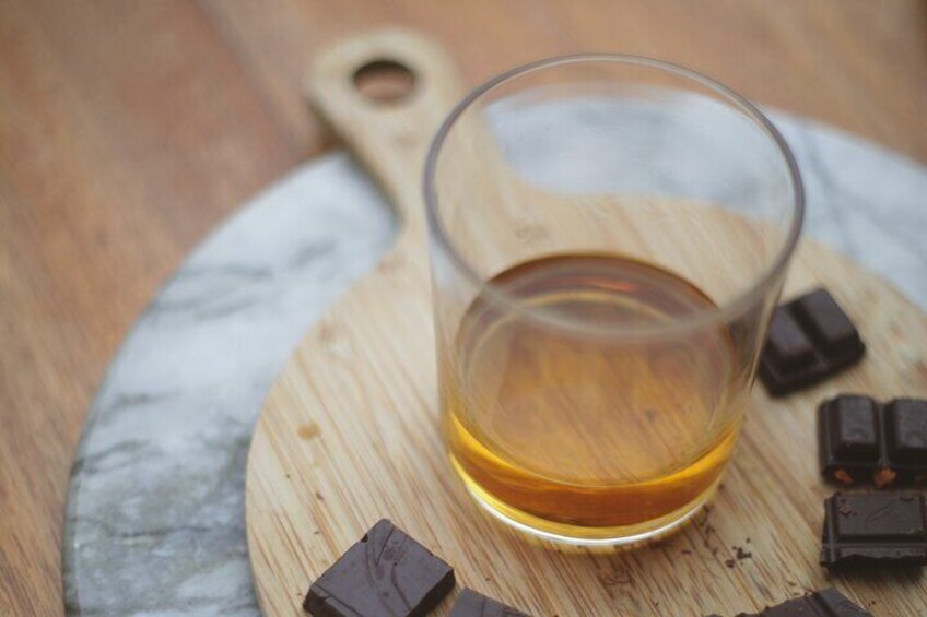 A glass of amber liquid on a wooden board with chocolate pieces. 1