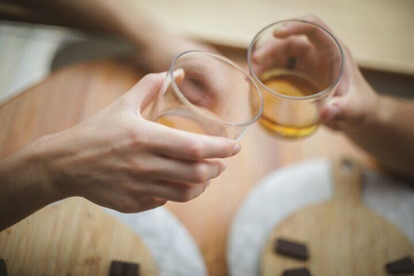 Two hands holding glasses of amber liquid, likely a beverage, with wooden barrels in the background. 4