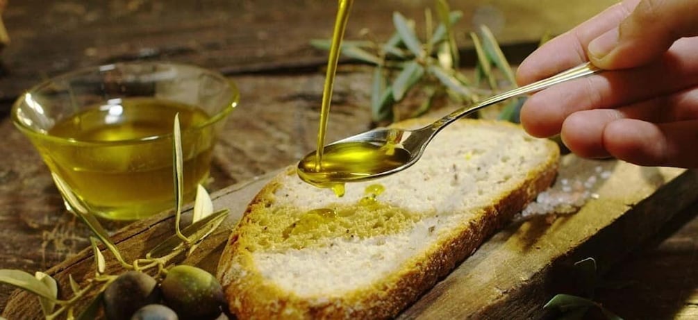 A hand pouring olive oil onto a slice of bread on a wooden board. 3