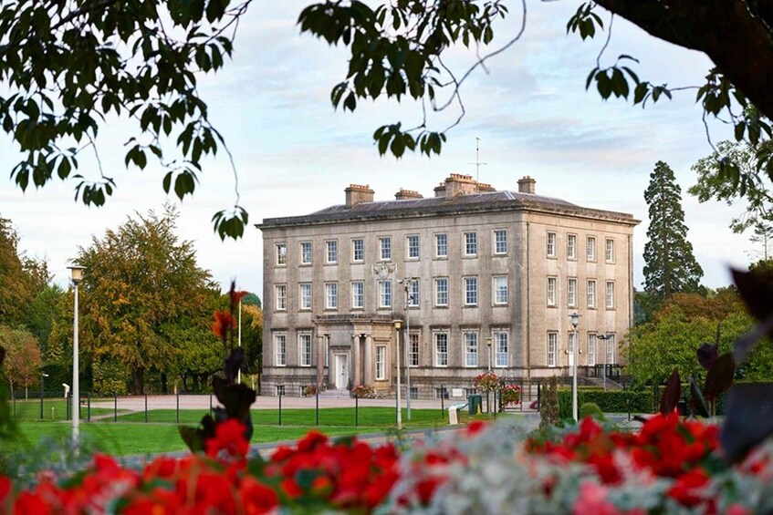 A large, historic building with a symmetrical facade, surrounded by a well-maintained garden with red flowers. 3
