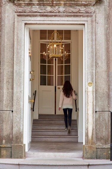 A woman walking up a grand staircase with a chandelier above the door. 2