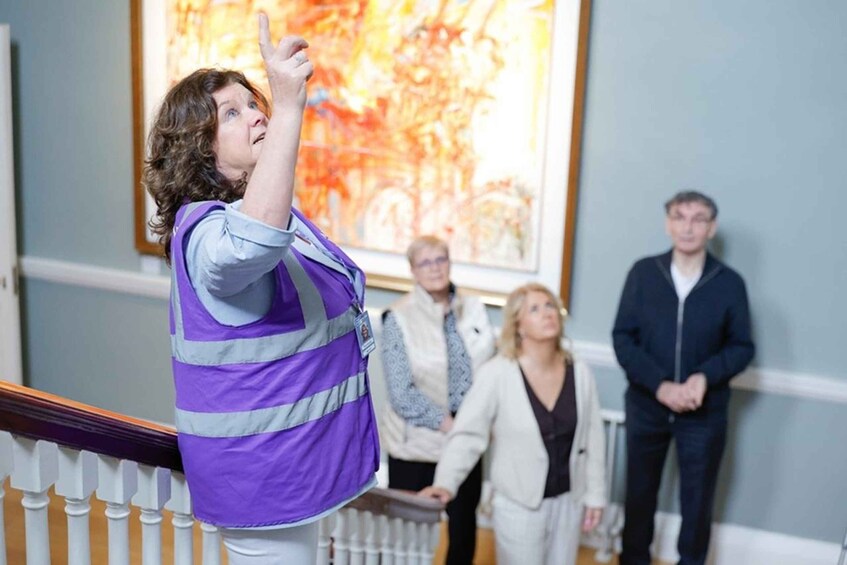A person in a purple vest pointing upwards, standing on a staircase with a railing. 1