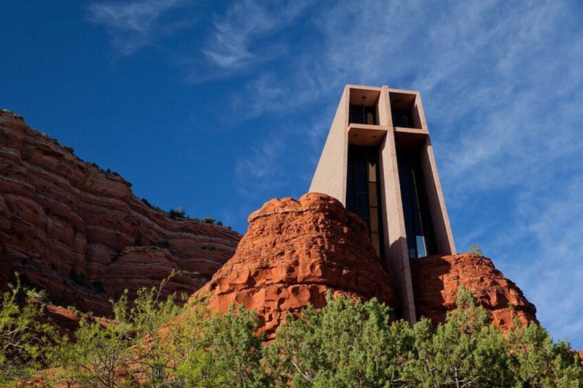 A building with a unique architectural design, situated on a red rock formation with green vegetation in the foreground. 2