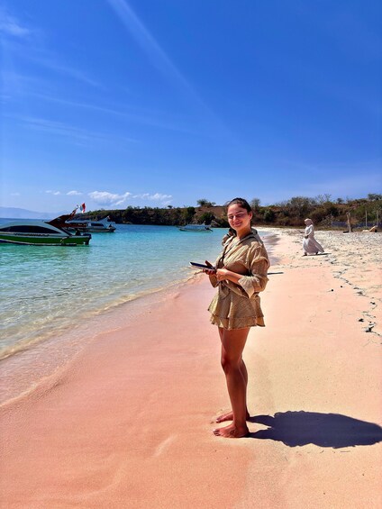 A beach with clear turquoise water, a person standing on the sand, and boats in the water. 1