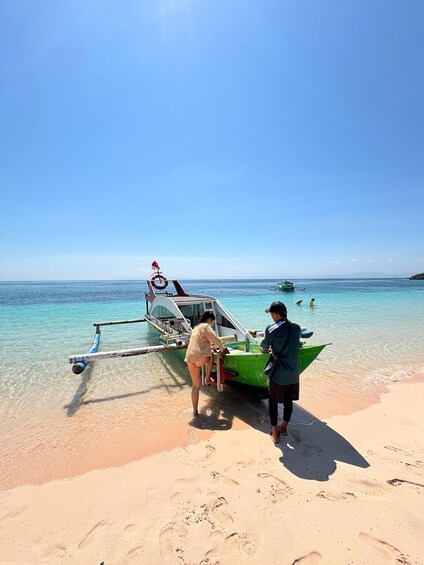A beach with a small boat, a person standing on the sand, and another person near the boat. 5