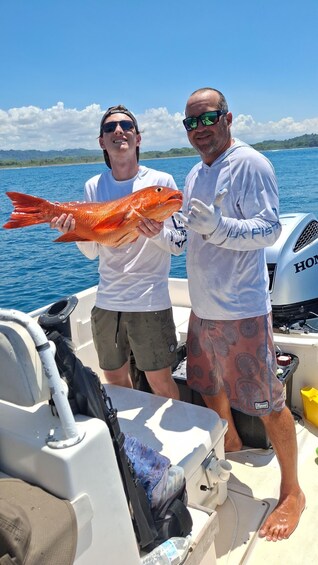 Two people on a boat holding a large fish, with a water body and distant land in the background. 5