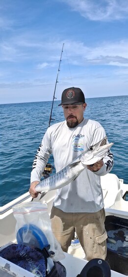 A person holding a large fish on a boat with a fishing rod in the background. 2