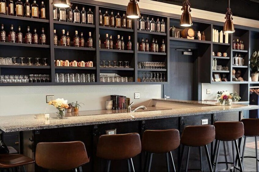 A bar with shelves of bottles, a bar counter, and brown chairs. 3