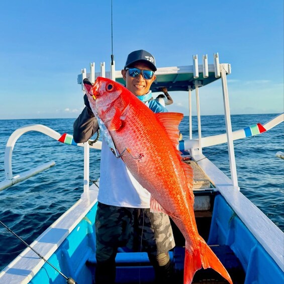 A person holding a large red fish on a boat. 1