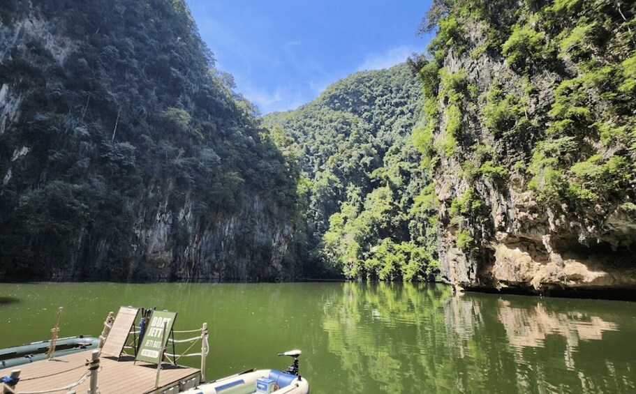 A boat docked at a calm river surrounded by steep cliffs and lush greenery. 1
