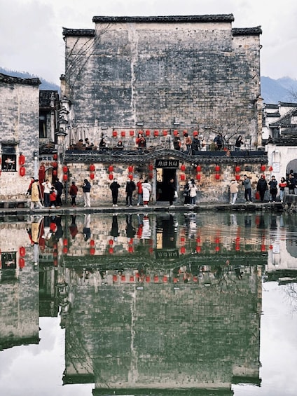 A traditional building with a reflection in the water, red lanterns, and people standing on the steps. 5