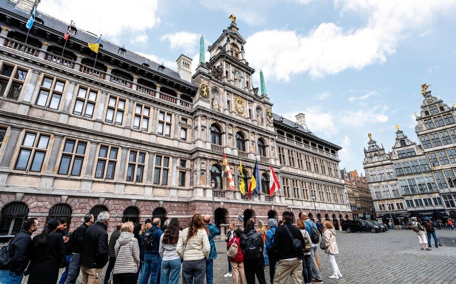 A historic building with ornate architecture, flags, and a crowd of people. 1