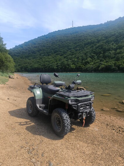 An ATV parked on a gravel path by a lake with a forested hill in the background. 5