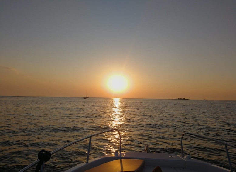 A boat at sunset with the sun reflecting on the water, a distant island, and a sailboat on the horizon. 5