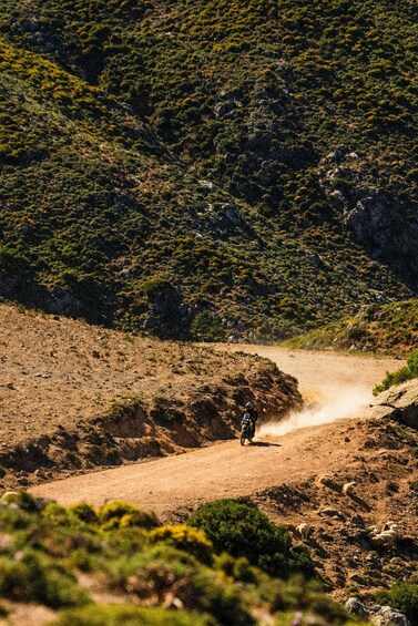 A dirt road winding through a hilly landscape with sparse vegetation and a motorcyclist riding away from the camera. 5
