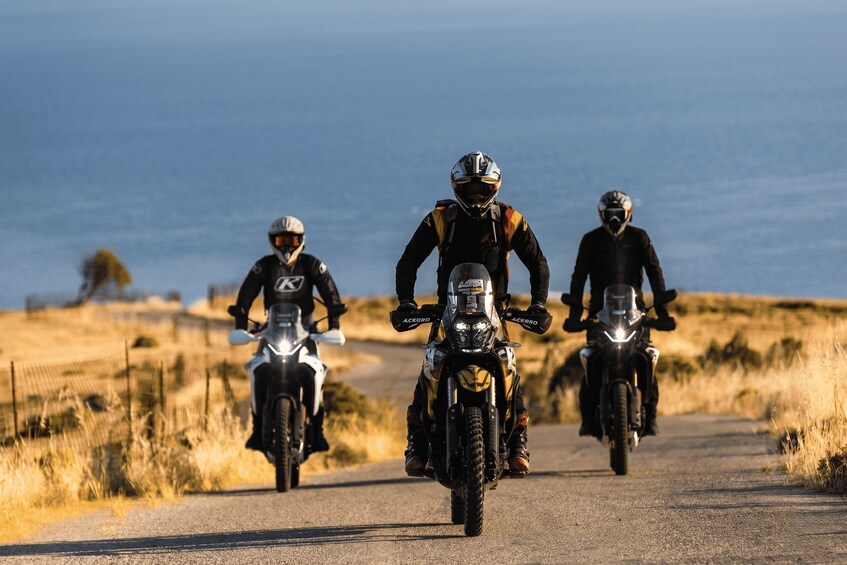 Three motorcyclists riding on a road with a coastal landscape in the background. 1