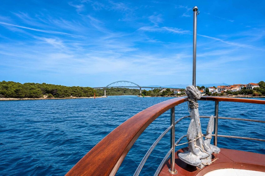 A boat's wooden railing with a metal anchor, a blue sea, and a bridge in the distance. 3