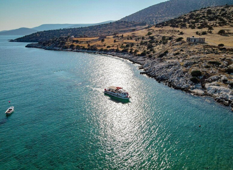 A boat on a turquoise sea with rocky shores and a hilly landscape in the background. 1