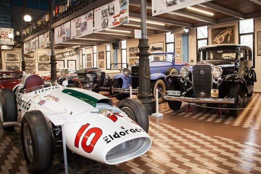 A vintage car museum with a white race car and a classic black car on display. 2