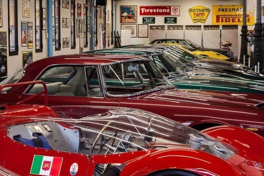 A collection of vintage cars in a garage with various brand signs on the wall. 3