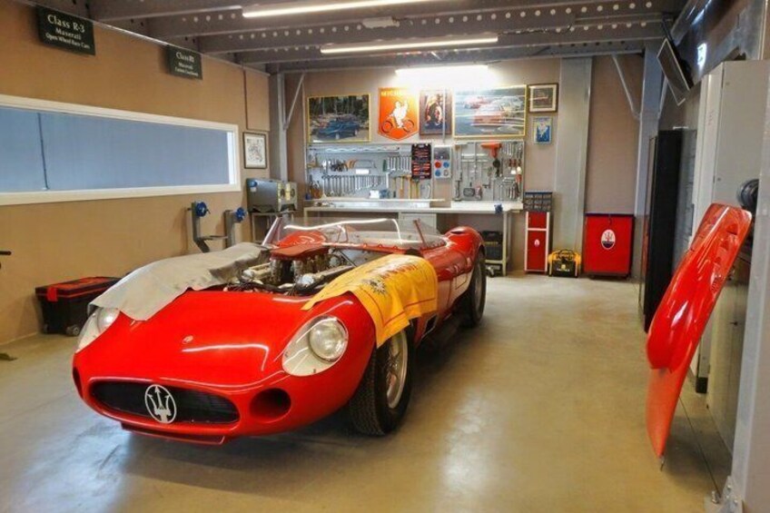 A red sports car in a garage with tools and equipment on the walls. 5
