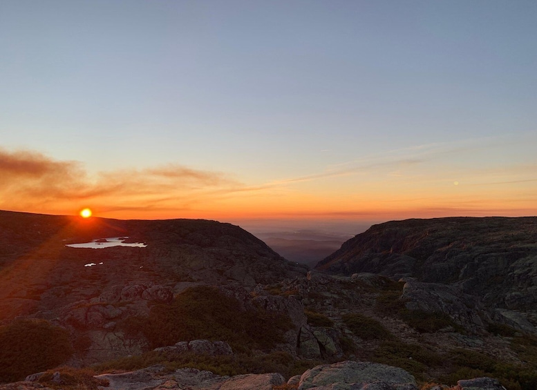 A mountain landscape at sunset with the sun setting between two rocky cliffs. 1