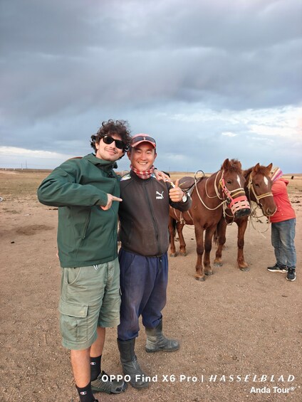 Two people with horses in a dry, open field under a cloudy sky. 3