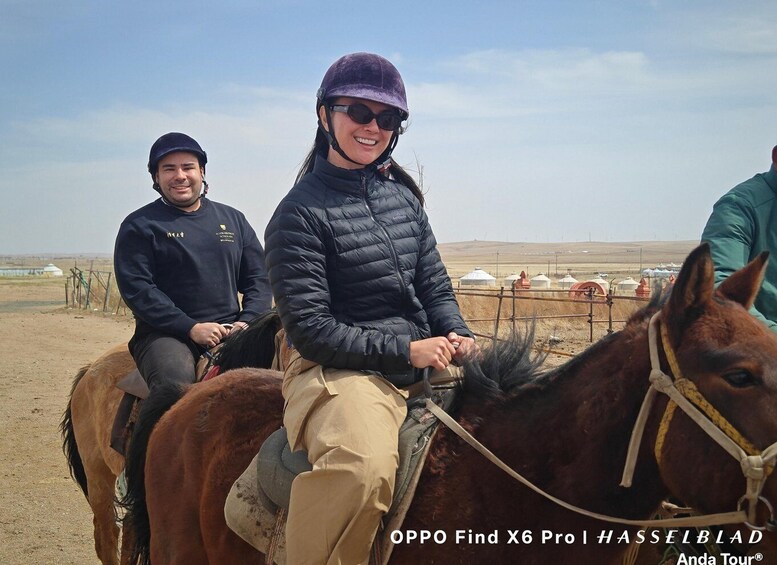 Two people riding a horse in a rural setting with yurts in the background. 4