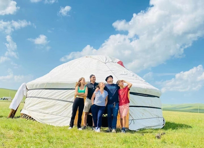 A group of people standing in front of a large white tent with a red stripe, set in a grassy field with a clear blue sky. 5