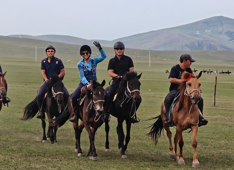 Four people riding horses in a grassy field with a mountain in the background. 1