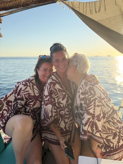 Three people on a boat with a patterned fabric, ocean, and a clear sky. 3