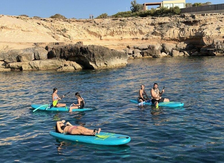 People on paddleboards in a calm body of water with rocky cliffs in the background. 1