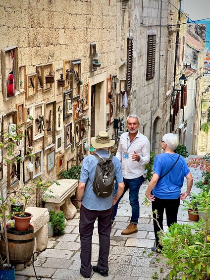 A narrow street with old buildings, a man with a backpack, and two other people walking. 1