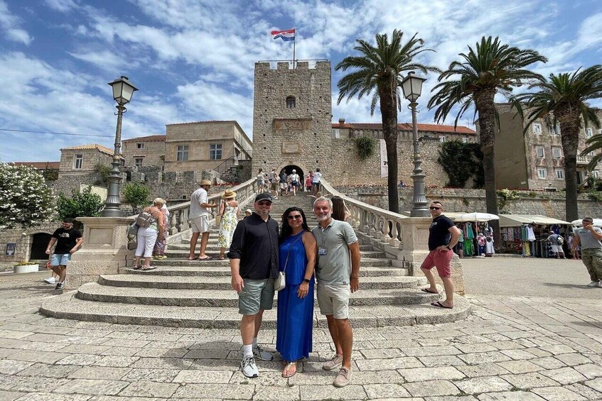 A historic stone tower with a flag, palm trees, and people on a stone staircase. 4