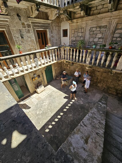 A courtyard with stone walls, a green door, and a balcony with white balustrades. 3