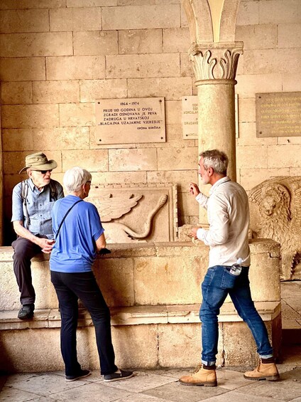 Three people examining a stone relief and inscriptions on a wall. 5