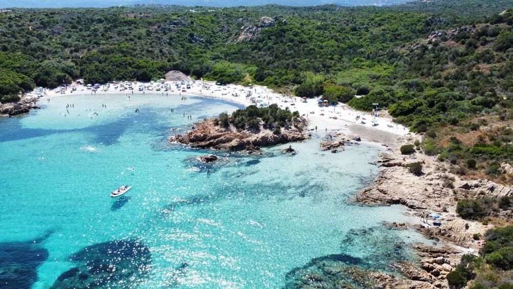 A coastal area with clear turquoise waters, a sandy beach, and a rocky outcrop surrounded by greenery. 2