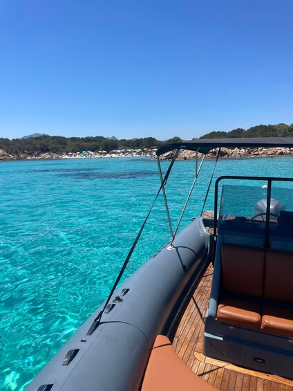 A boat on clear turquoise water with a rocky beach and trees in the background. 3