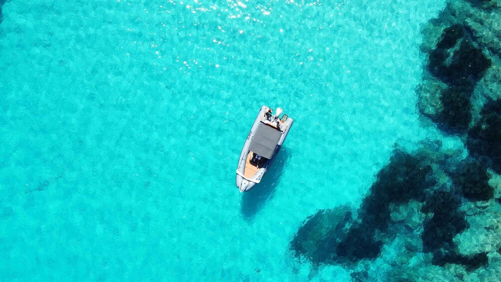 An aerial view of a boat on clear turquoise water with visible underwater rock formations. 1