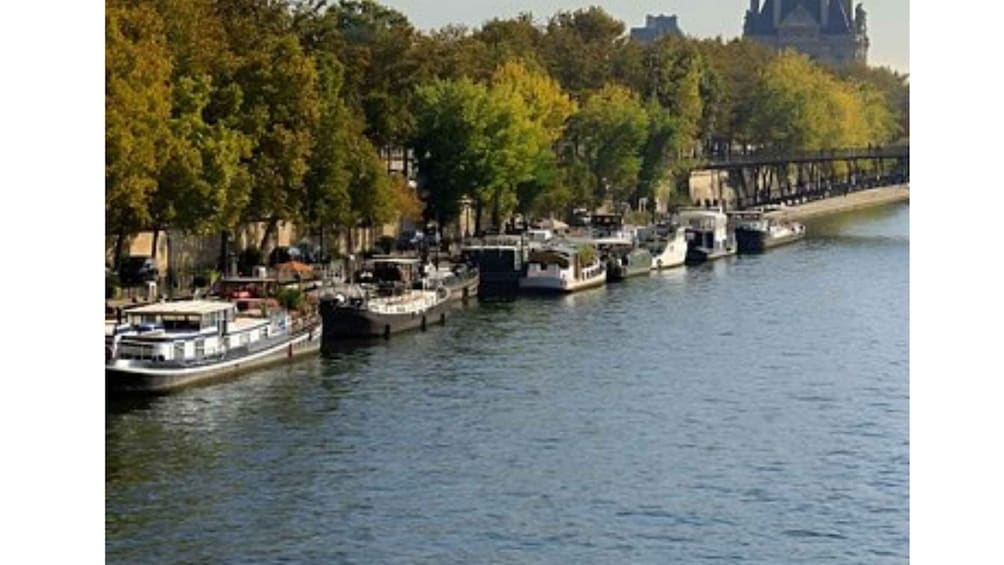 A river with boats docked along the banks, trees lining the shore, and a bridge in the background. 5