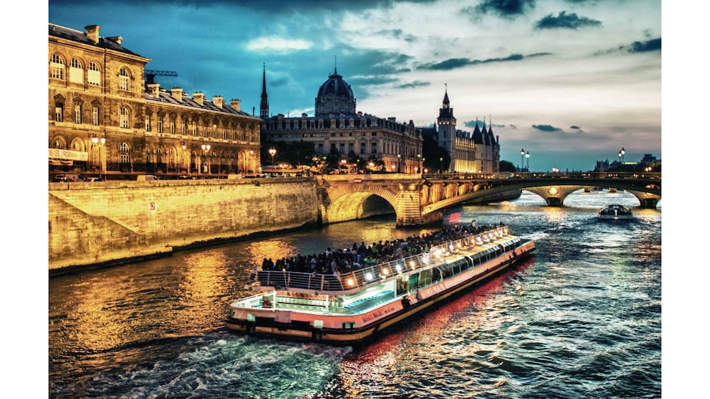 A river with a boat carrying passengers, a bridge, and historic buildings. 4
