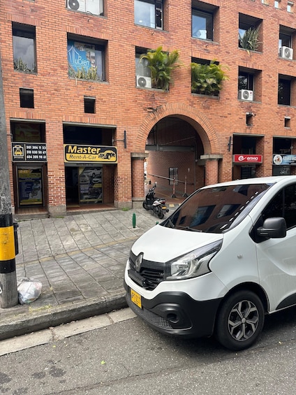 A white car parked in front of a brick building with multiple businesses, including a car rental service. 2