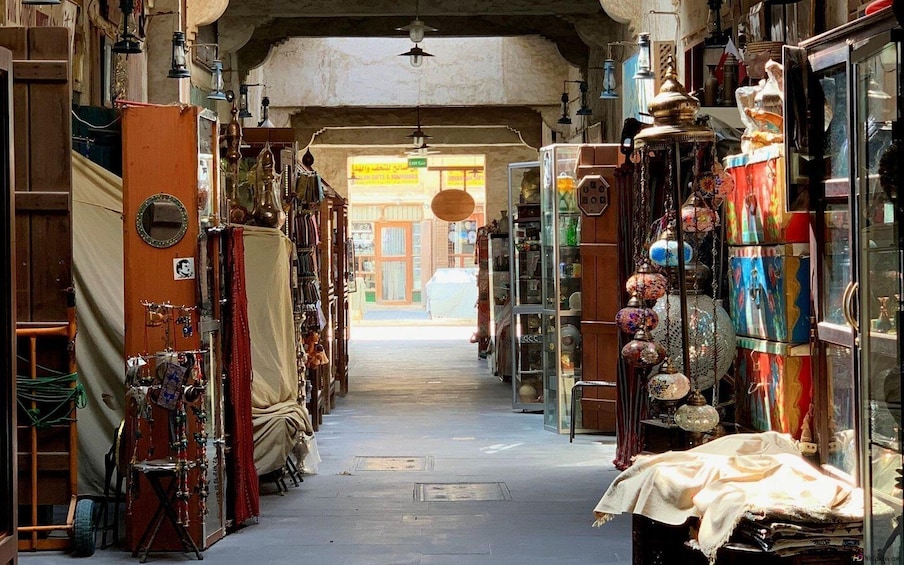 A narrow street lined with various shops displaying an array of items including textiles, pottery, and decorative objects. 3
