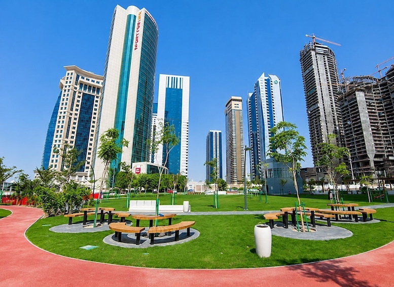 A cityscape with modern high-rise buildings, a park with picnic tables, and a clear blue sky. 4