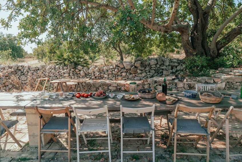 An outdoor dining area with a stone wall, wooden chairs, and a table set with food and drink. 5
