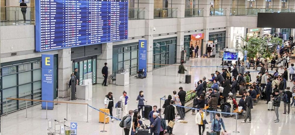 A busy airport terminal with an electronic flight information display and a large crowd of travelers. 1
