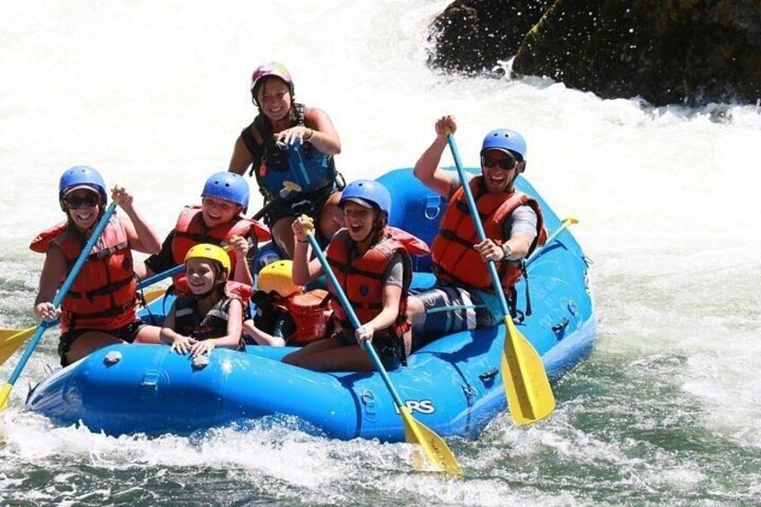 A group of people in a blue inflatable raft on a river, wearing life jackets and helmets. 1