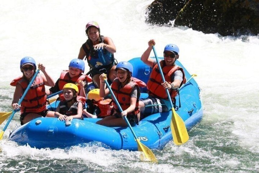 A group of people in a blue raft on a river with rapids. 1