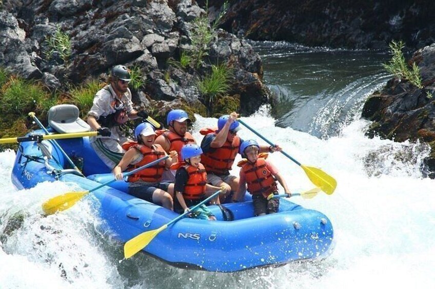 A group of people in a blue raft navigating a river with rapids. 2